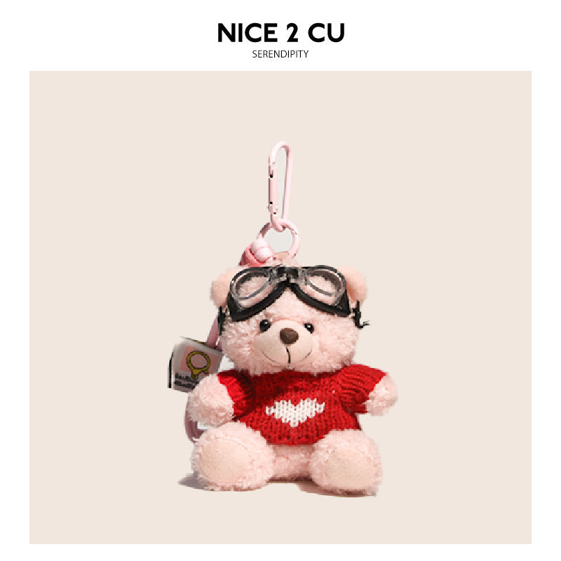 Pink teddy bear bag charm in a red knitted sweater with white heart motif and black aviator goggles