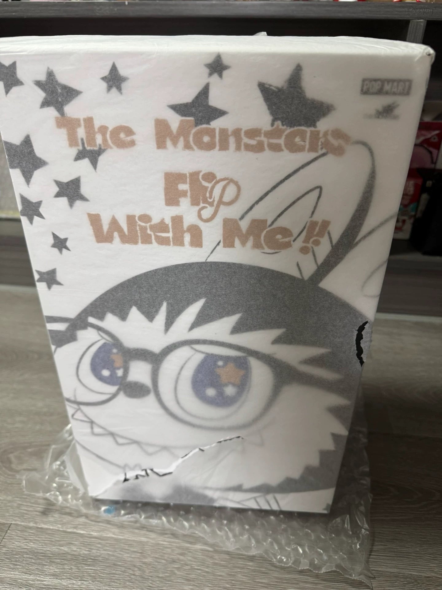 A rectangular POP MART box with a cartoon Labubu in glasses, stars, and "The Monsters Flip With Me!" on the front contains the 38cm Labubu Vinyl Plush Doll in Sailor Shirt & Denim—an art collectible displayed on a wooden floor.
