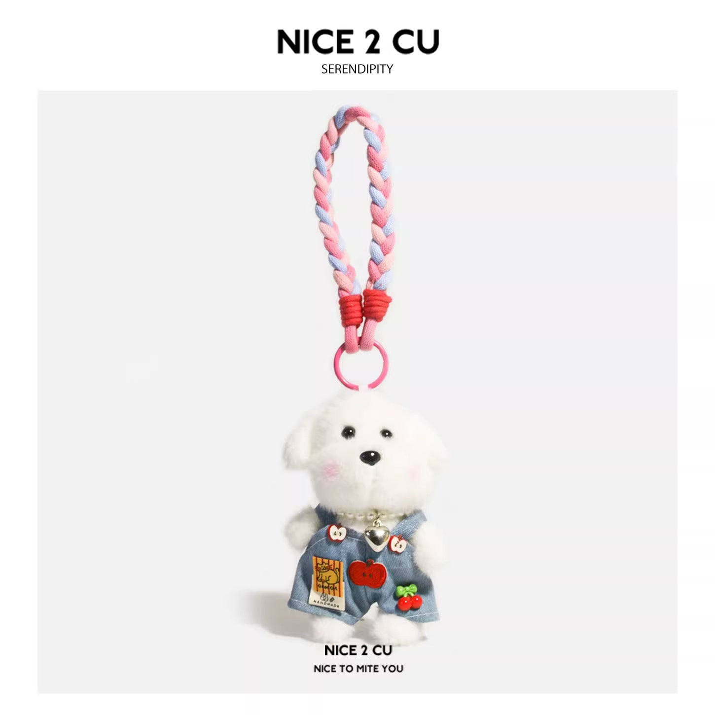 White plush dog charm in blue denim-style overalls with fruit-themed patches and braided pink-blue strap