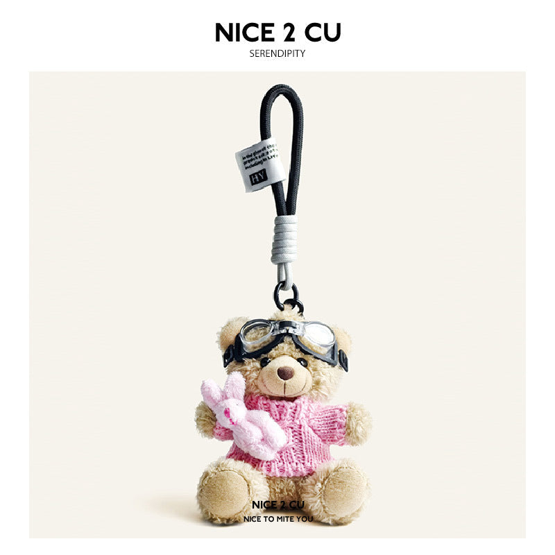 Beige plush teddy bear keychain in light pink knit sweater with aviator goggles, holding a small pink rabbit