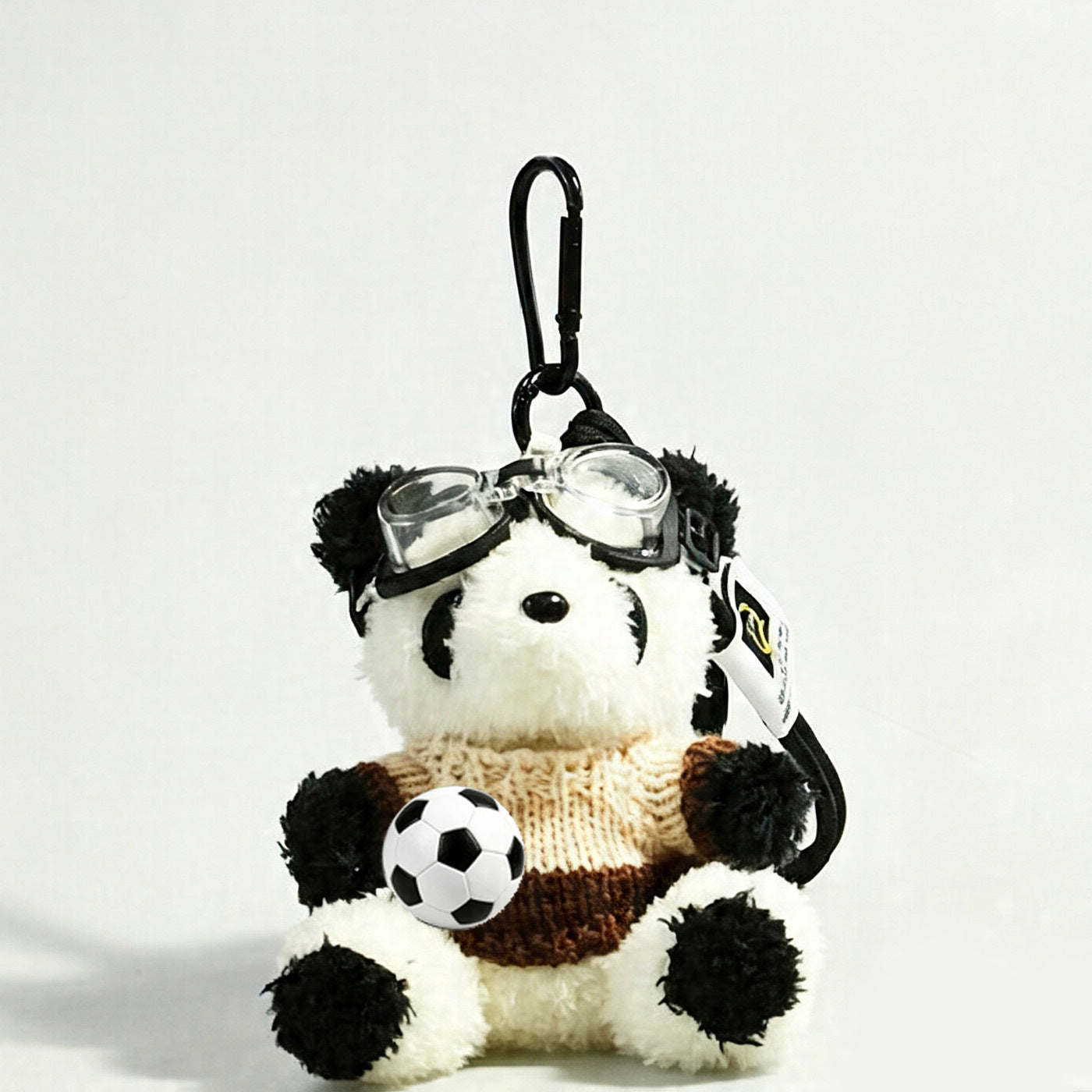Panda plush keychain in a cream and brown coffee-toned knit sweater with clear goggles and soccer ball prop