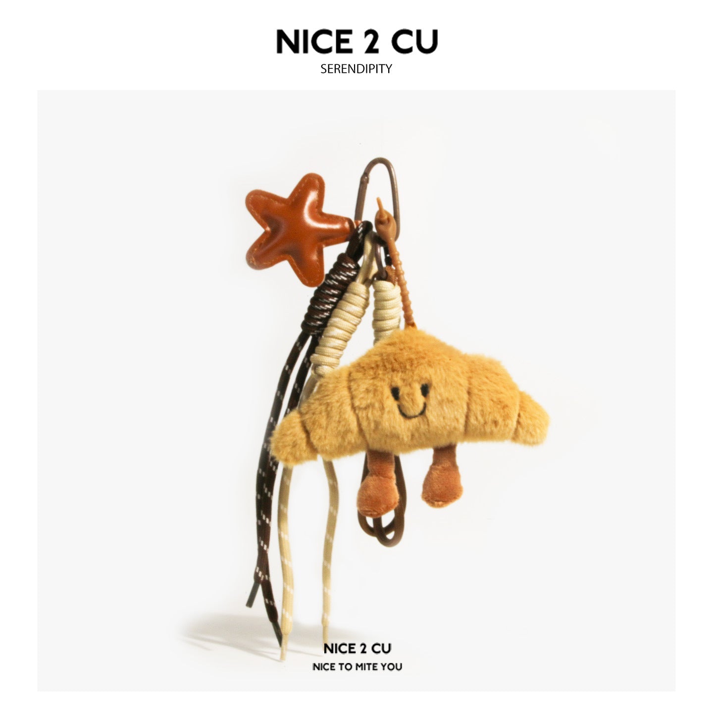 Golden croissant plush keychain charm with embroidered smiley face, star accent charm, and braided cords on metal carabiner c