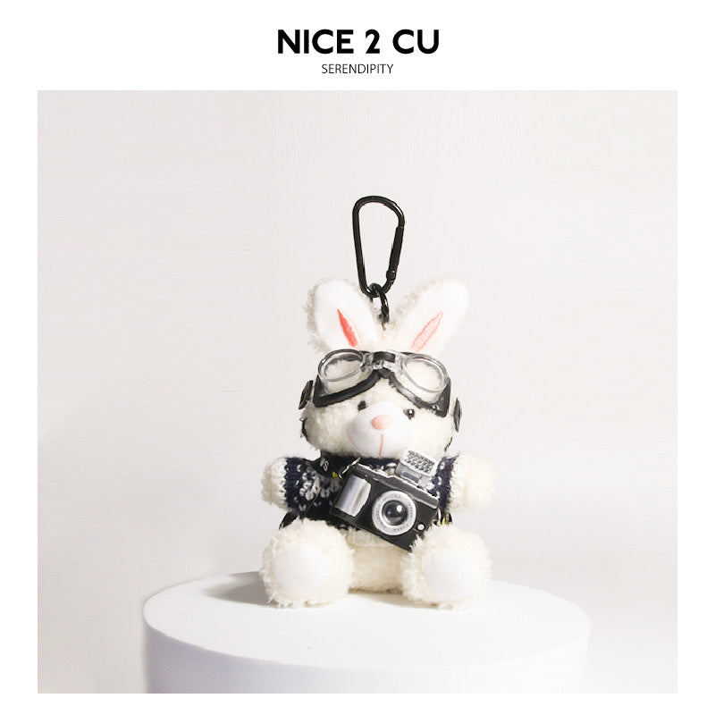 White plush rabbit keychain wearing blue-and-black knit sweater with aviator goggles and camera charm