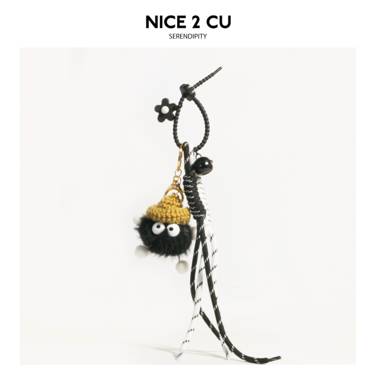 Black fluffy googly-eye character charm with mustard-gold crocheted hat, black flower bead, and black-and-white braided tasse