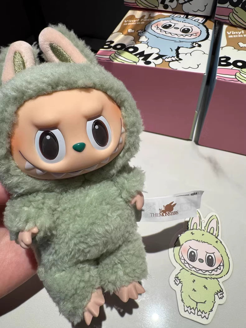 A hand holds the POP MART Labubu “Green Grape” Plush Keychain from The Monsters Standing Green Bunny series. Matching packaging, a character tag, and this collectible bunny plush keychain appear in the background.