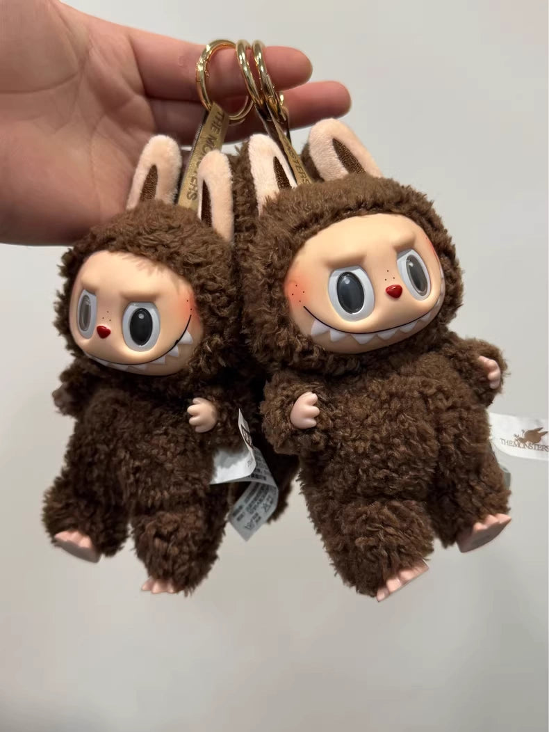A hand holds two POP MART Labubu Secret Edition "Chestnut Cocoa" Plush Keychains—standing brown bunnies by Kasing Lung, featuring large eyes and playful grins inspired by the collectible vinyl series.