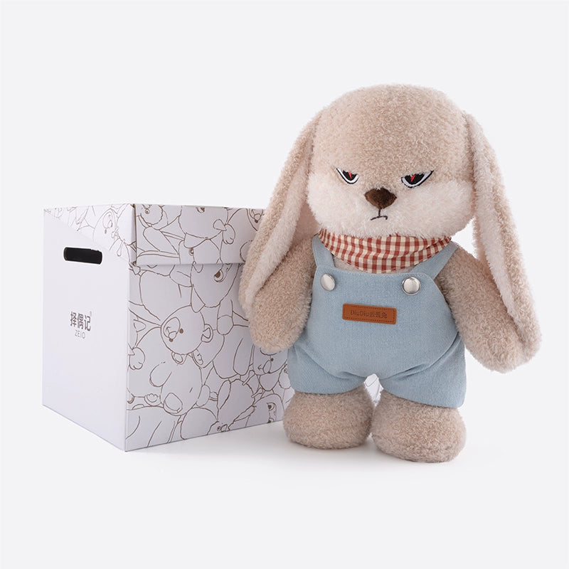 The ZEIO Bunny Plush Toy 35cm, a soft rabbit in denim overalls and striped scarf, stands by a white handled box with bunny illustrations—an adorable nursery décor piece.