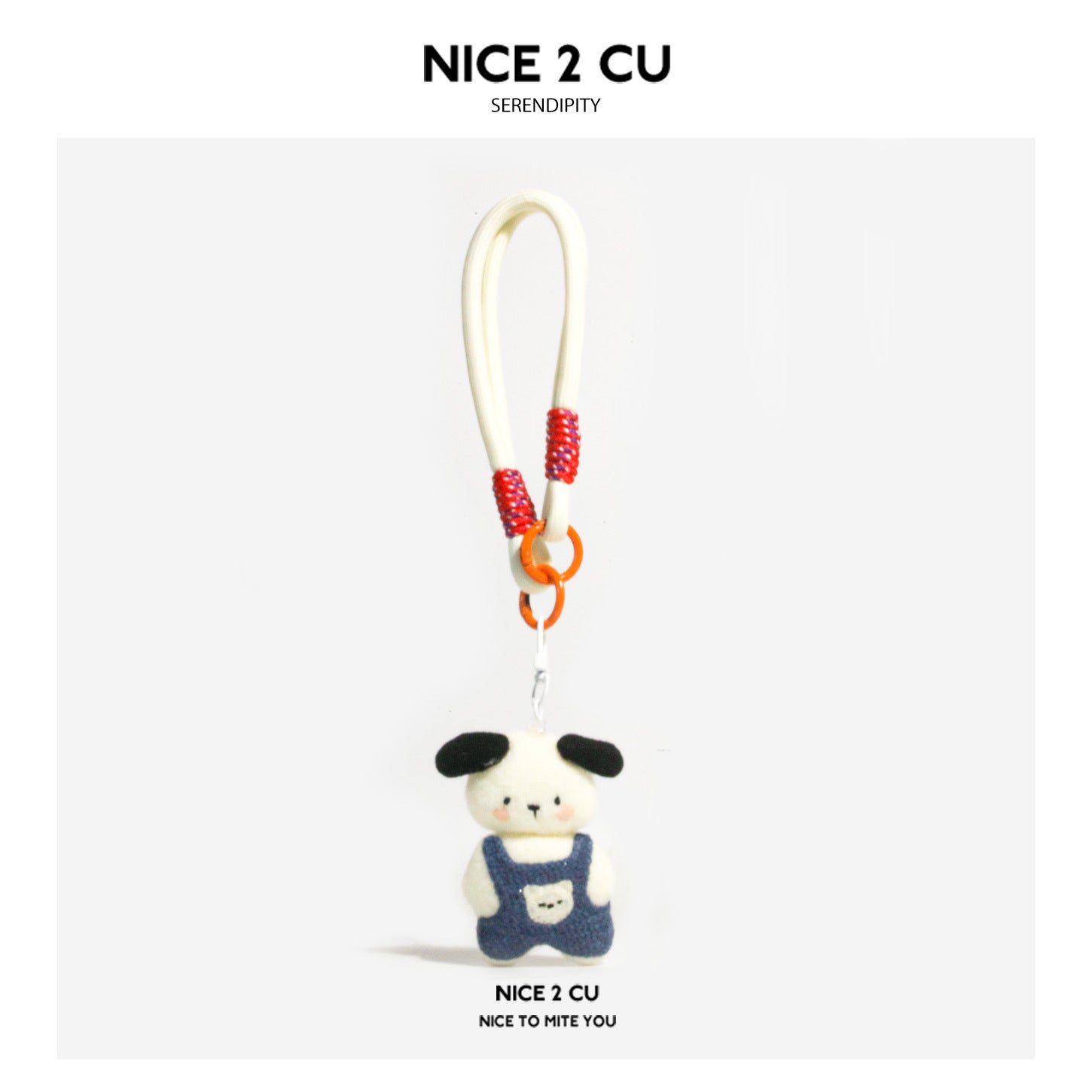 Small white and black plush dog charm in blue overalls on a red and orange braided cord loop keychain
