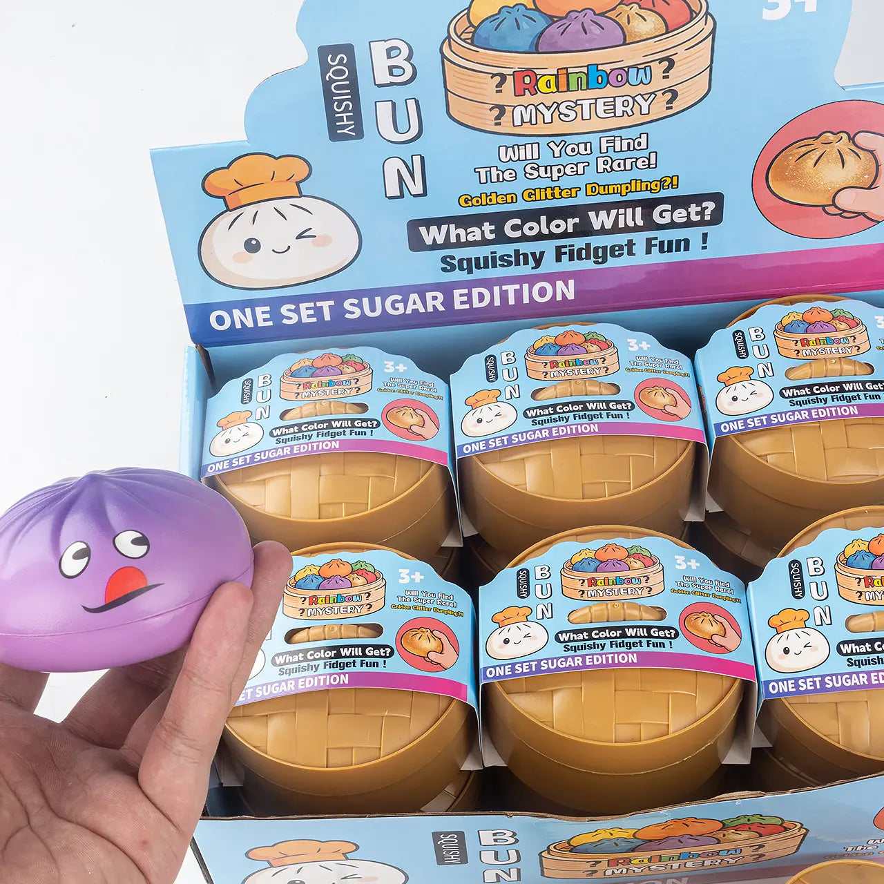A hand holds a ZoDoll Giant Emoji Squishy Dumpling Bun Sensory Fidget Toy with Steamer—Rainbow Mystery Squeeze Ball, perfect for stress relief and sensory fun for kids and adults. Kawaii expressions add playful charm.