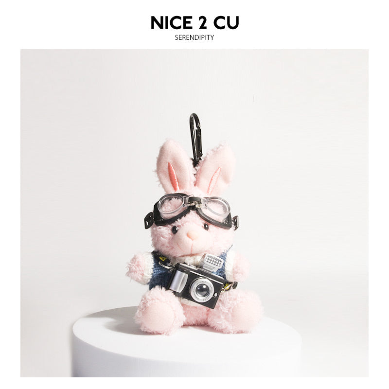 Pink plush rabbit keychain wearing blue-and-white knit sweater, aviator goggles, and holding a miniature retro camera