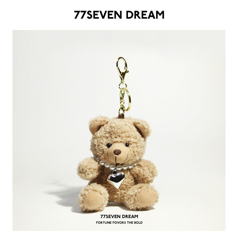 Beige teddy bear plush keychain accessorized with a pearl-style necklace and heart pendant, gold-tone clip