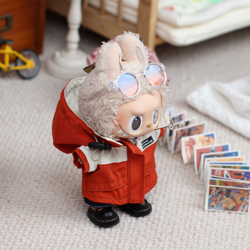 A ZoDoll Labubu plush wears the Red Explorer Jacket Outfit Set with gloves and boots, featuring a color-block parka with a fuzzy hood and ears plus round glasses, standing on carpet by miniature illustrated cards.