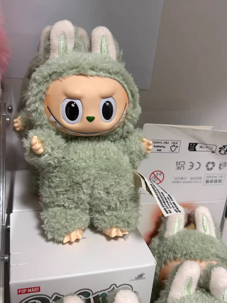 A POP MART Labubu “Green Grape” Plush Keychain from The Monsters series, featuring a standing green bunny, is on display with similar dolls and keychains lined up behind it.
