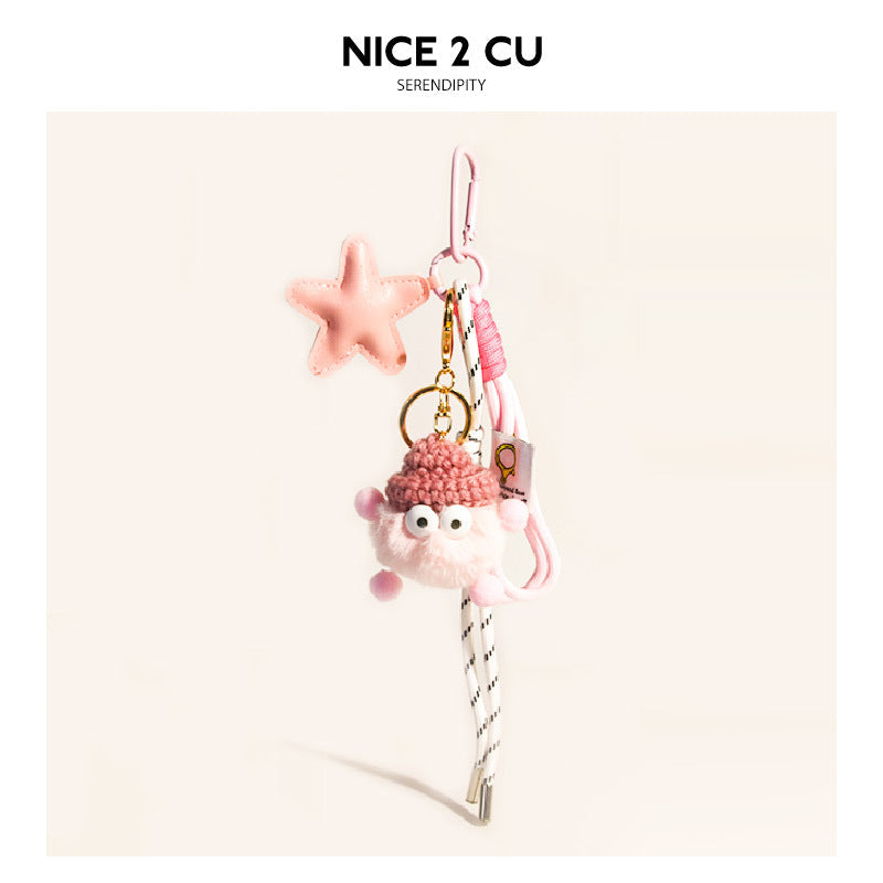 Pink and white fluffy character bag charm with pink knit hat, pale pink star pendant, pink braided cord, and gold clip