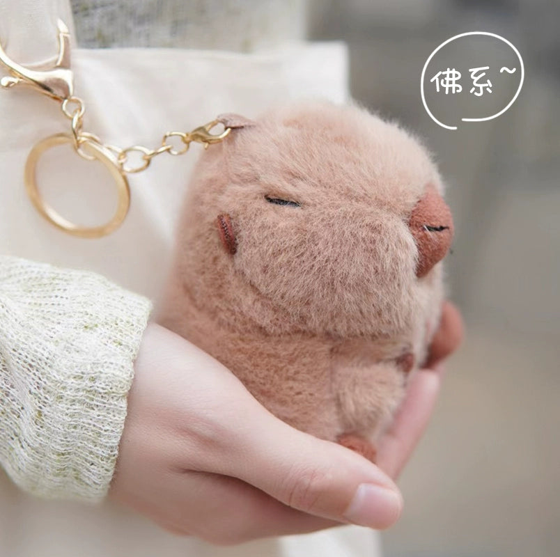 Someone holds the ZEIO Guinea Pig Plush Keychain 11cm—a soft mini cavy keyring charm with gold hardware—while white Chinese characters in the background enhance its adorable appeal.