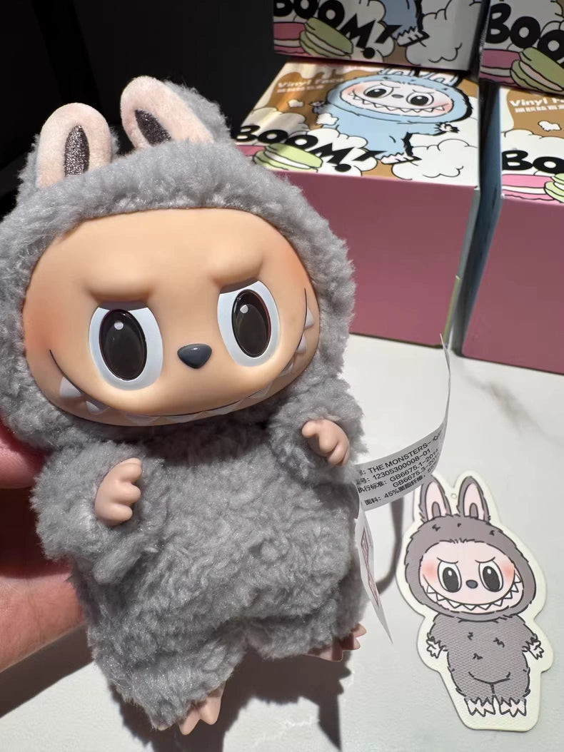 A hand holds the POP MART Labubu “Sesame Bean” Plush Keychain—Standing Grey Bunny by Kasing Lung—beside a matching sticker and two colorful Pop Mart Sesame Bean boxes in the background.