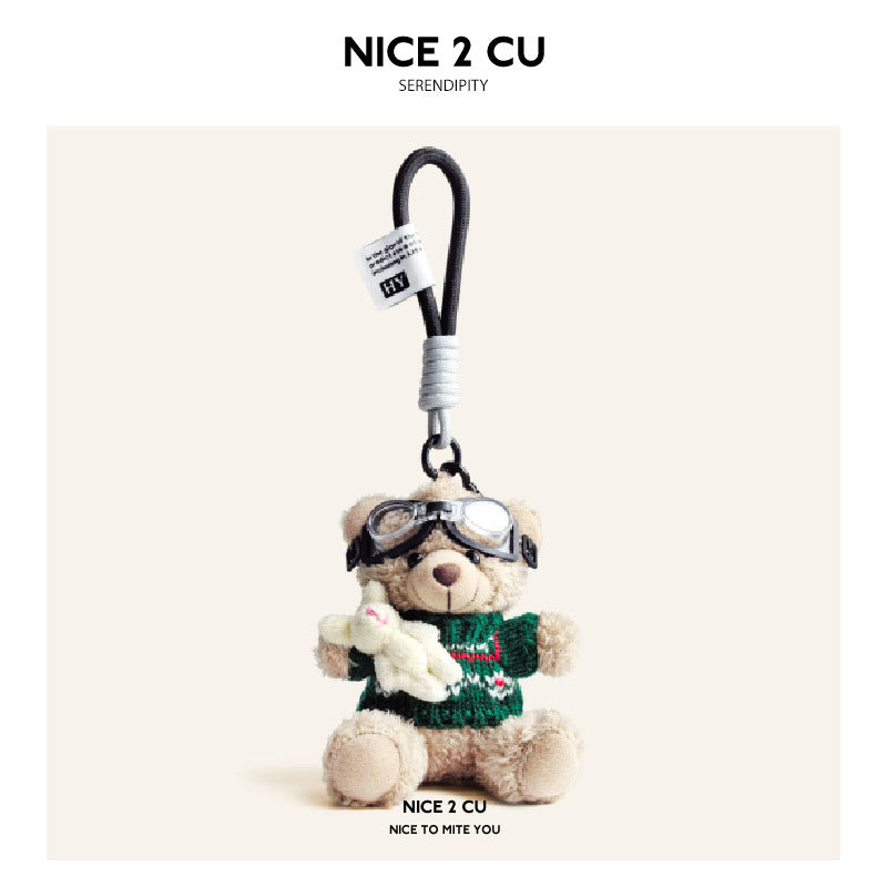 Beige plush teddy bear keychain in green patterned knit sweater with aviator goggles, holding a white rabbit