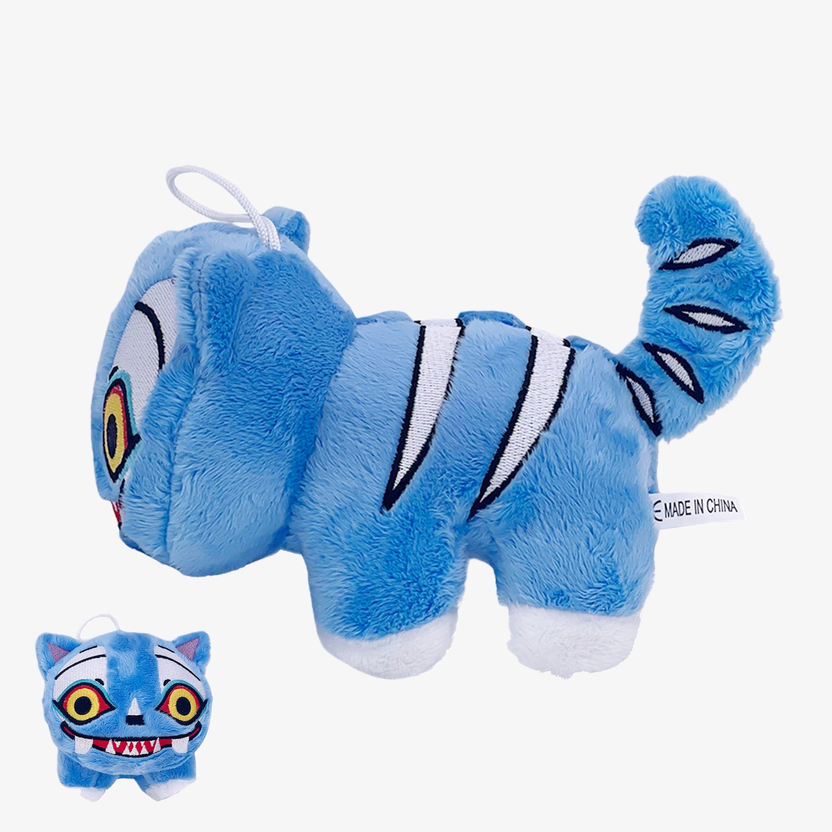 The Demon Hunters Monster Plush Doll is a 7-inch blue tiger creature with a striped tail, wide cartoon eyes, and a hanging loop. A smaller version of this soft stuffed toy by Demon Hunters appears in the bottom left corner.