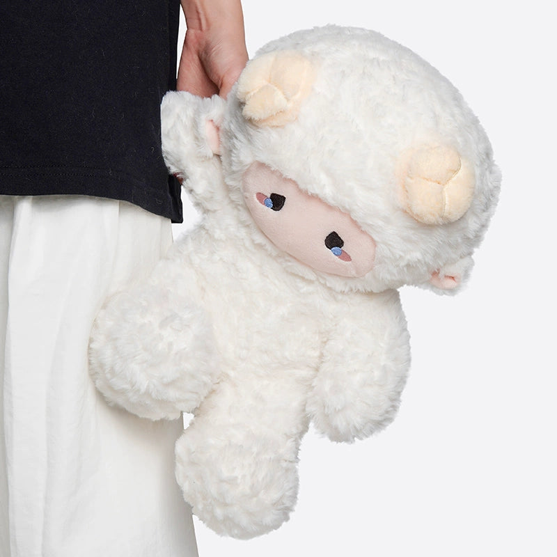 A person holds a ZEIO Fashion Sheep Plush Toy 29cm—a cute dressed lamb doll with accessories, featuring fluffy white fur and cream-colored horns. The person wears a black top and white pants.