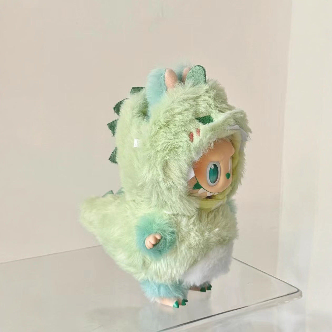 A ZoDoll Labubu Green Monster Bunny Plush Hoodie Doll Costume Outfit is displayed on a clear platform against a plain background.