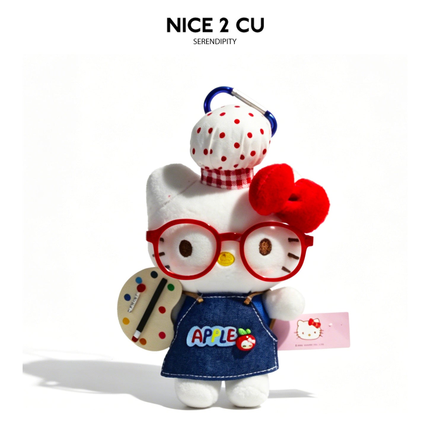 Hello Kitty-style plush charm in denim apron with red glasses, polka-dot hat, and painter's palette accessory