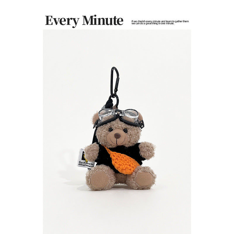 Brown bear plush keychain charm wearing aviator goggles, a black knit sweater, and an orange front accessory with black carab