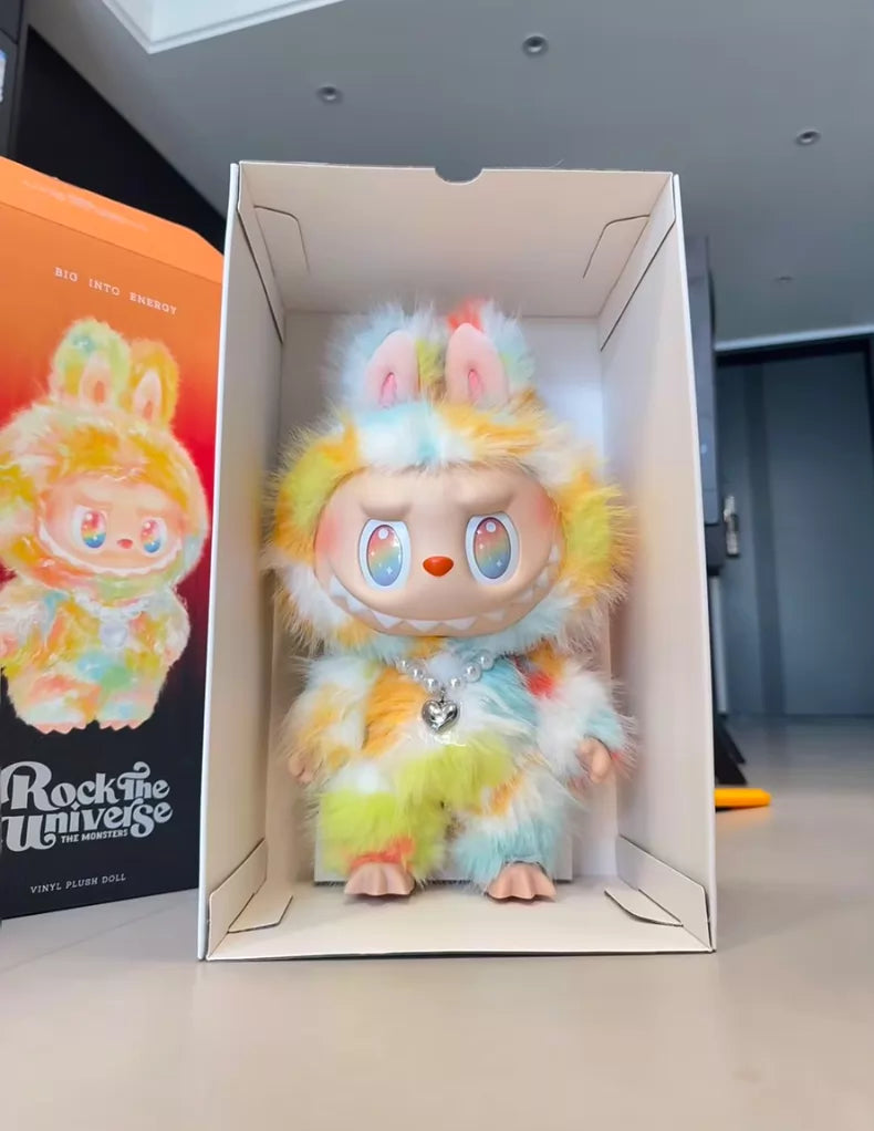 The Labubu Big into Energy Series Plush Doll – 37cm from POP MART stands upright in an open box beside its packaging, featuring large eyes and pastel fur. It’s a designer collectible from the Pop Mart THE MONSTERS collection.