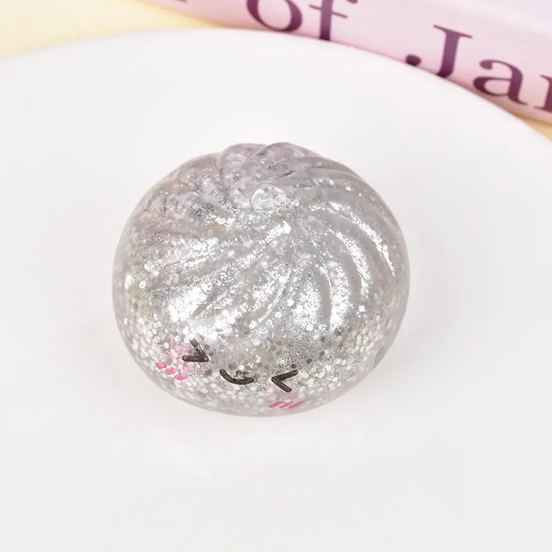 The ZoDoll Glitter Squishy Dumpling Sensory Fidget Toy, shaped like a dumpling with a cute blushing face, sits in its included steamer plate.