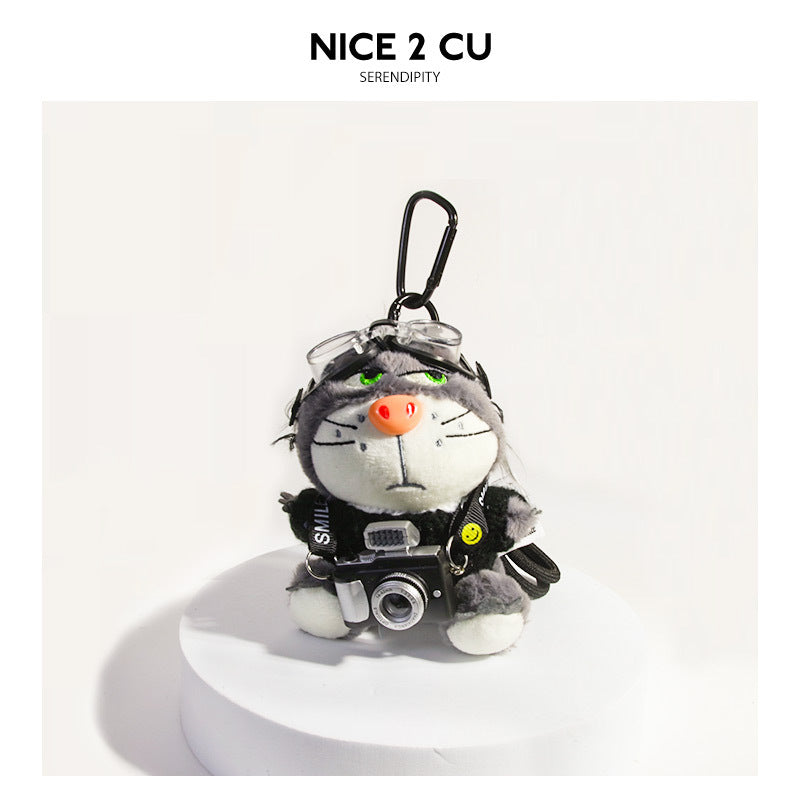 Gray and white plush cat keychain charm in black sweater holding miniature camera with carabiner clip