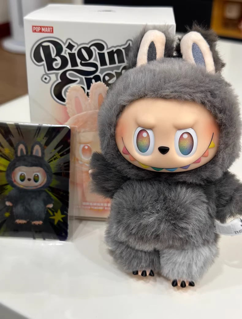 The POP MART Labubu “Secret Edition” Plush Keychain from The Monsters “Big Into Energy” Series, featuring gray bunny ears and rainbow-colored eyes, stands before its packaging and collectible card on a white surface.