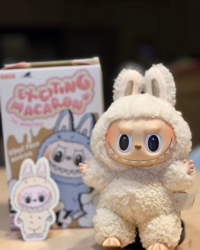 A Labubu “Soymilk” Plush Keychain – Pop Mart The Monsters Beige Bunny Doll by POP MART stands in front of its Exciting Macaron box, which features matching character art and a small sticker beside it.