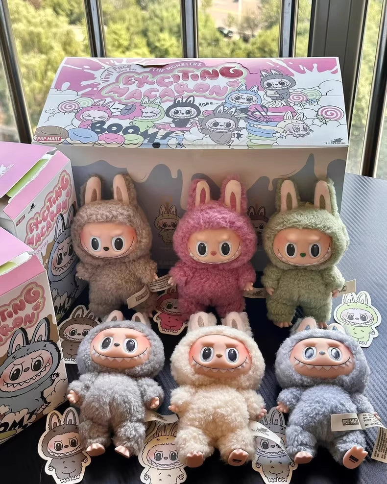 The POP MART Labubu The Monsters “Exciting Macaron” complete 6-piece plush keychain set, featuring limited edition vinyl face bunny dolls, is displayed with matching character stickers in front of its colorful box near a window.