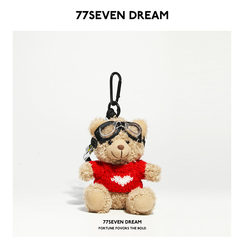 Beige teddy bear plush keychain wearing a bright red knit shirt with a white heart and aviator goggles