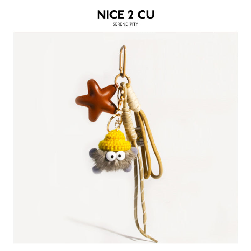Cream and grey fluffy character bag charm with yellow knit hat, star charm, braided cream cord, and gold clip hardware