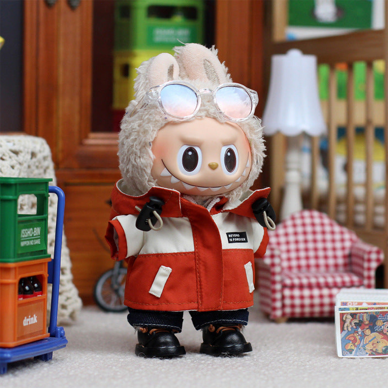 A ZoDoll Labubu plush doll in the Red Explorer Jacket Outfit Set with gloves and boots stands indoors near a crate, chair, lamp, and a small box featuring colorful artwork.