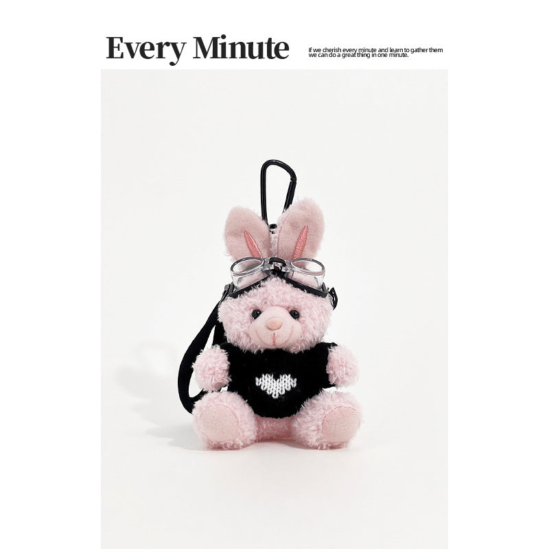 Pink rabbit plush keychain charm wearing aviator goggles and a black sweater with white heart motif and black carabiner clip