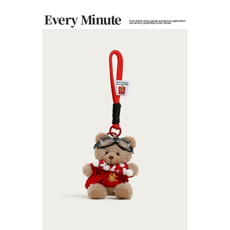 Brown plush teddy bear charm with red gold-character sweater, striped scarf, aviator goggles, and red mini backpack accessory