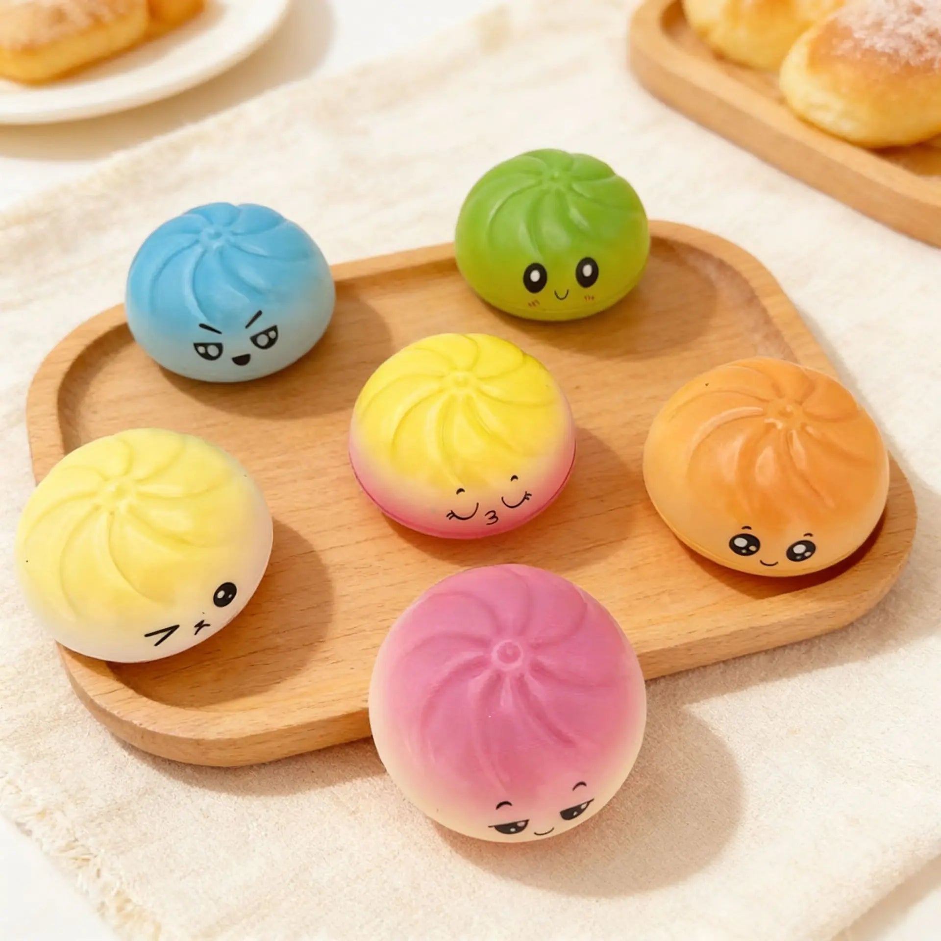 Six giant emoji squishy dumpling buns by ZoDoll are arranged on a wooden tray, each featuring a unique rainbow color and kawaii expression. Includes a steamer. A fun sensory fidget toy for stress relief—great for both kids and adults!.