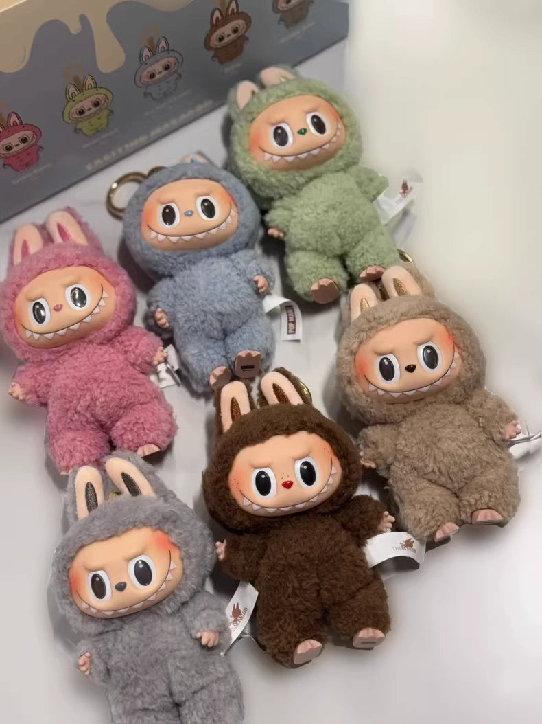 Six POP MART Labubu The Monsters “Exciting Macaron” plush keychains (complete 6-piece set) with vinyl bunny faces are arranged on a white surface, with the Pop Mart limited edition box featuring Kasing Lung’s bunny illustrations behind.