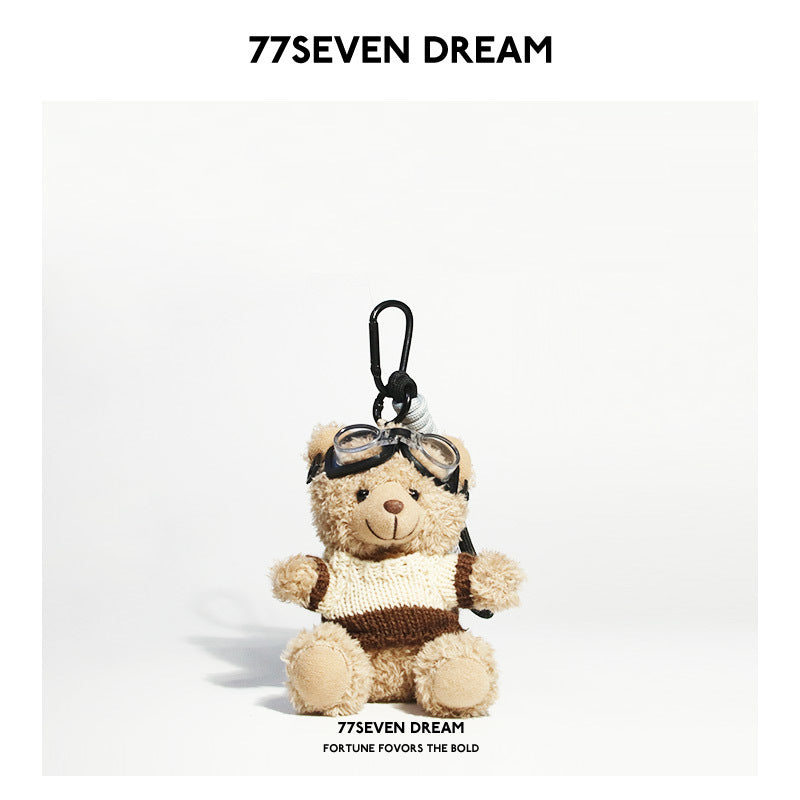 Beige teddy bear plush keychain in a cream-and-brown color-block knit sweater with aviator goggles