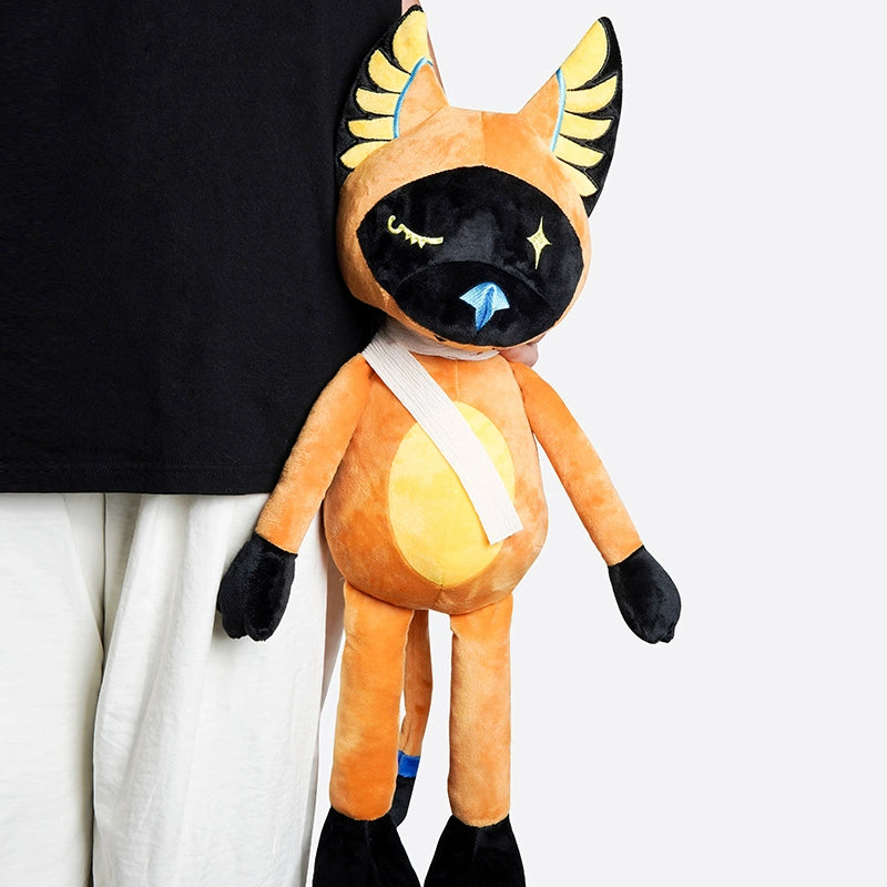 A person in white pants and a black shirt holds the ZEIO Egyptian Cat Plush Toy – a mystical stuffed animal with star eyes, yellow wings on its head, and a white strap around its neck.