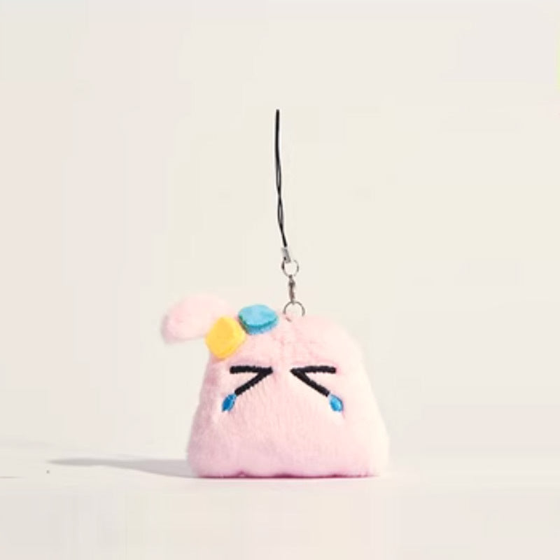 Pink chibi blob plush charm with drooping ear, X eyes, blue teardrop embroidery, and yellow-teal hair clip on black strap