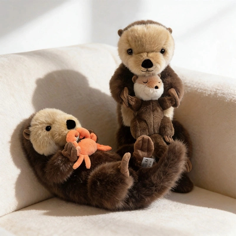 Two ZoDoll Otter Plush Toys (40x12cm) sit on a cream chair; one holds a removable plush crab, while the other cuddles a baby sea otter plush.