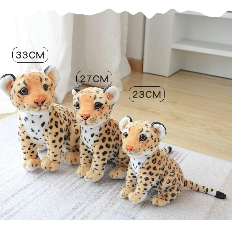 Three ZoDoll Cheetah Plush Animal Stuffed Toys (23cm, 27cm, and 33cm) are displayed in a row on a wooden floor near a curtain and white shelf, showcasing the soft, realistic cheetah dolls.