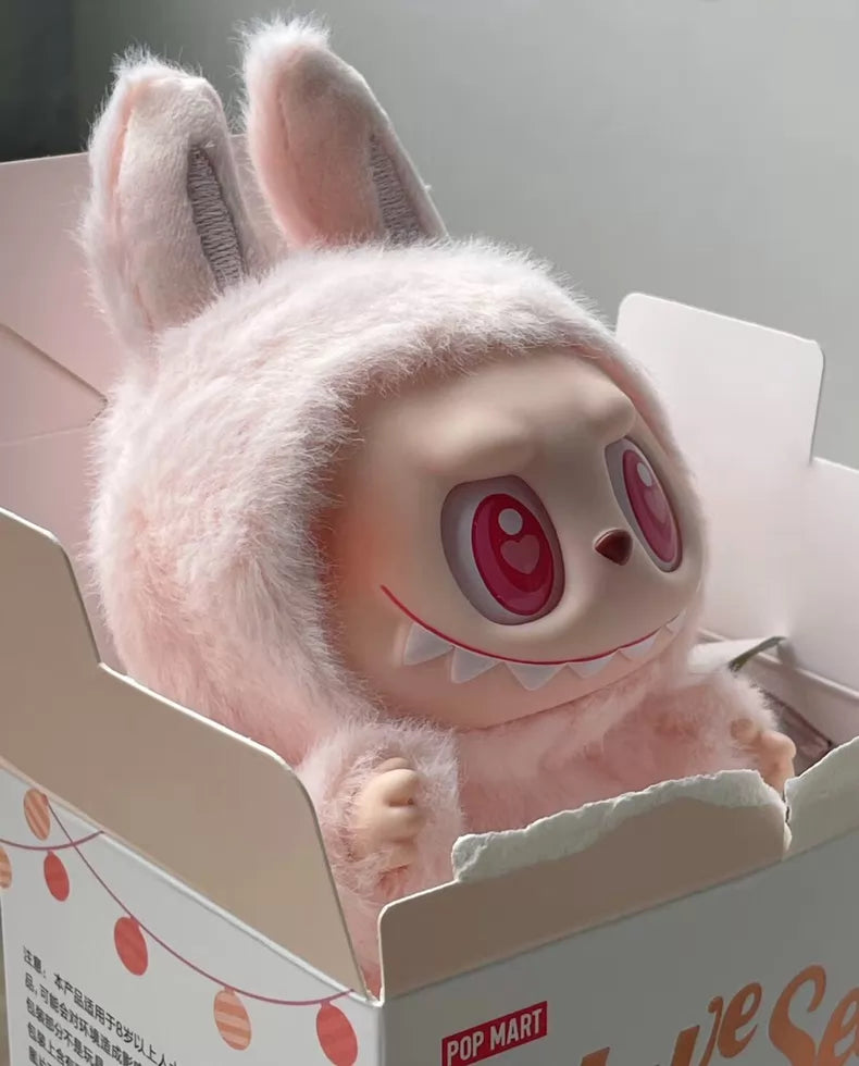 The Labubu “Dada” Plush Keychain – Have a Seat Series Pink Heart-Eye Bunny by Pop Mart The Monsters is a POP MART collectible featuring heart-shaped eyes, bunny ears, and fluffy pink fur, featured partially seated in an open box.