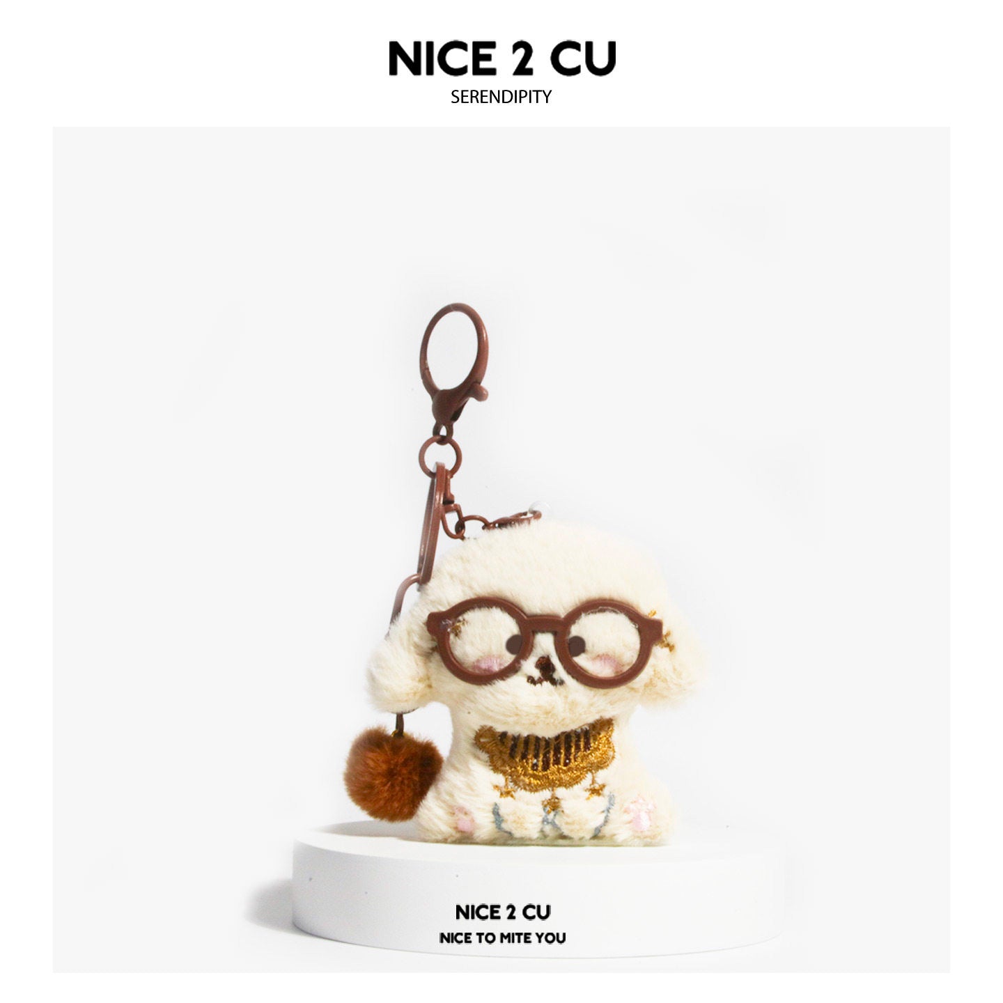 Cream plush dog keychain charm wearing round brown-framed glasses with gold embroidered chest panel and brown pom-pom