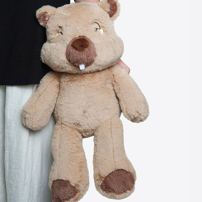 A person holds a large, light brown ZEIO Wombat Plush Toy (48cm), an ultra-soft stuffed animal featuring a big nose, two front teeth, dark brown accents on its paws and face, and includes a mini doll.