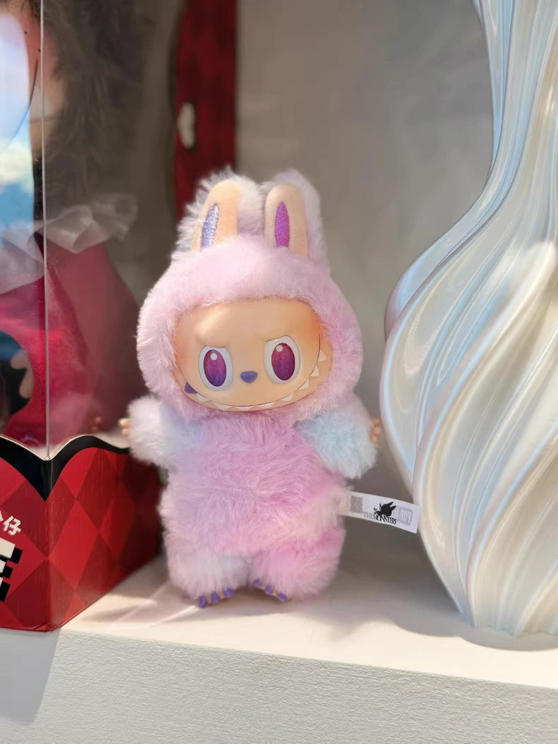 The POP MART Labubu “Luck” Plush Keychain from The Monsters “Big Into Energy” Series, featuring a pastel pink and purple bunny costume, hangs on a shelf among other items as an adorable bag charm.