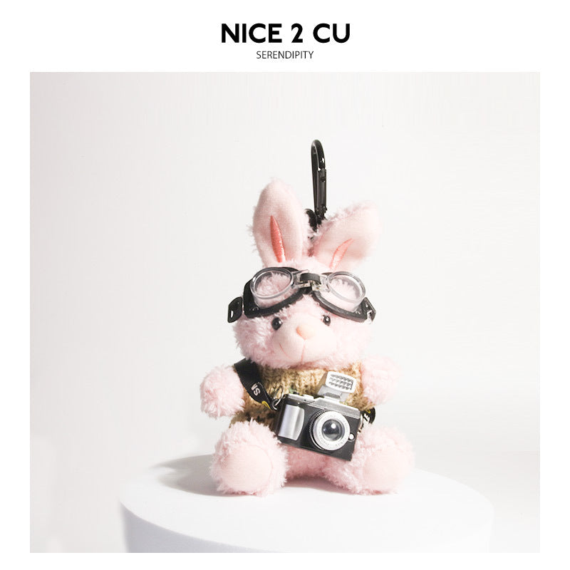 Pink plush rabbit keychain wearing khaki knit sweater with aviator goggles and small camera charm