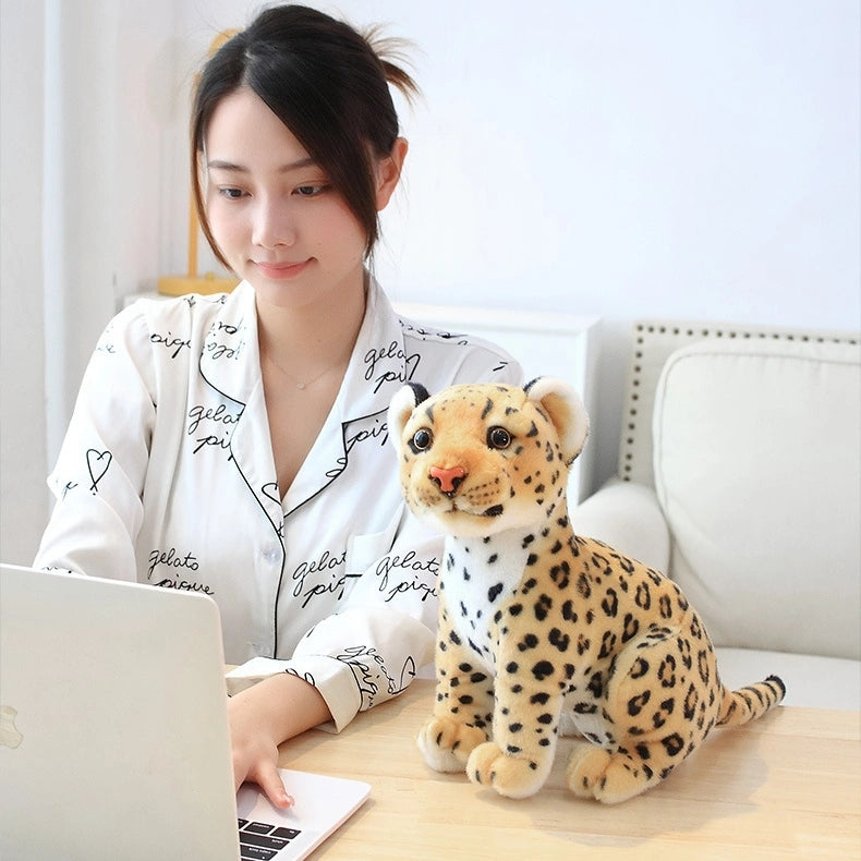 A woman in a white shirt works on a laptop at her desk, with a ZoDoll Cheetah Plush Animal Stuffed Toy (23cm, 27cm, or 33cm) sitting beside her.